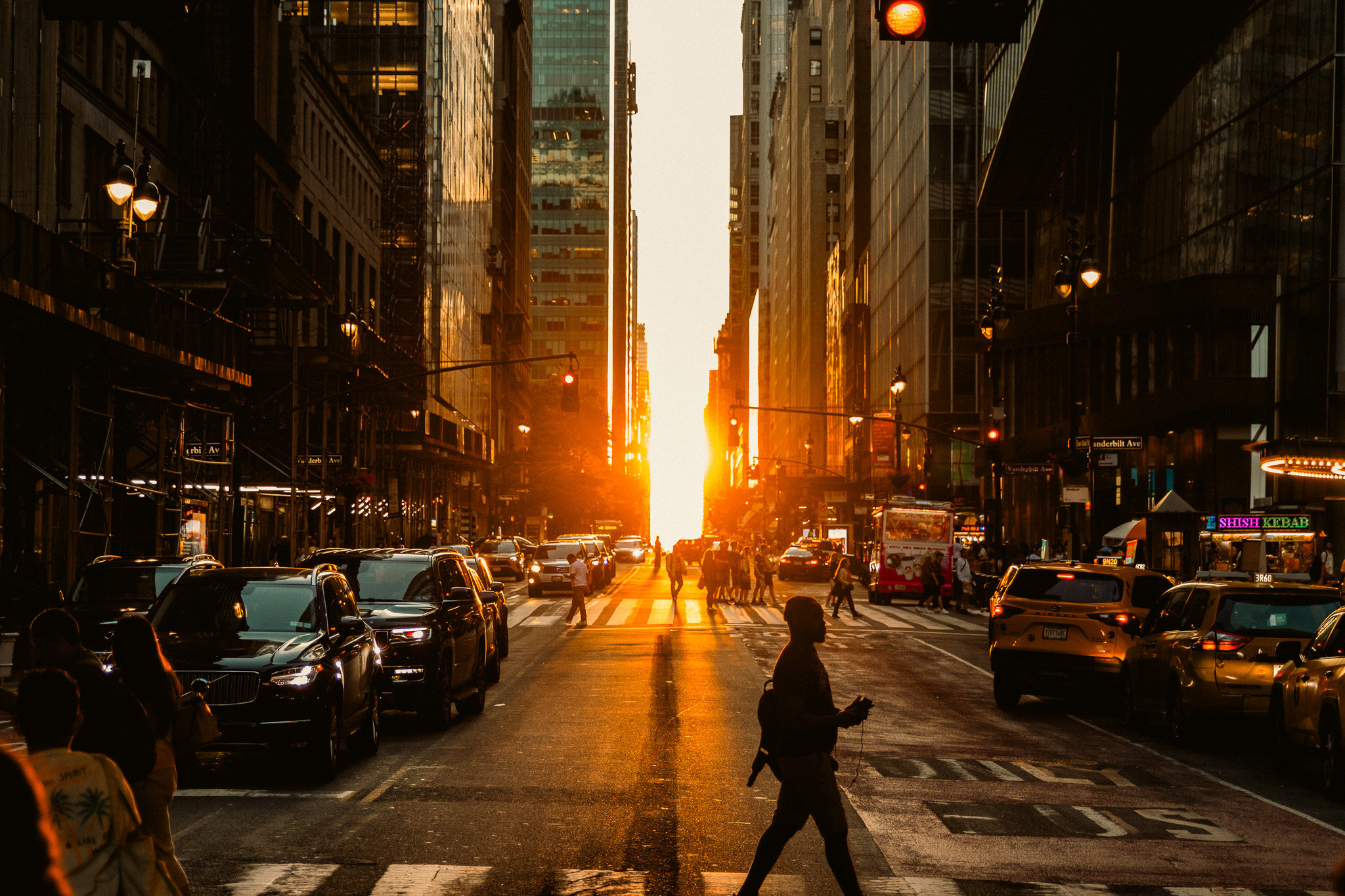 The setting sun aligned down a Manhattan cross street at Manhattanhenge, traffic and pedestrians silhouetted against the light