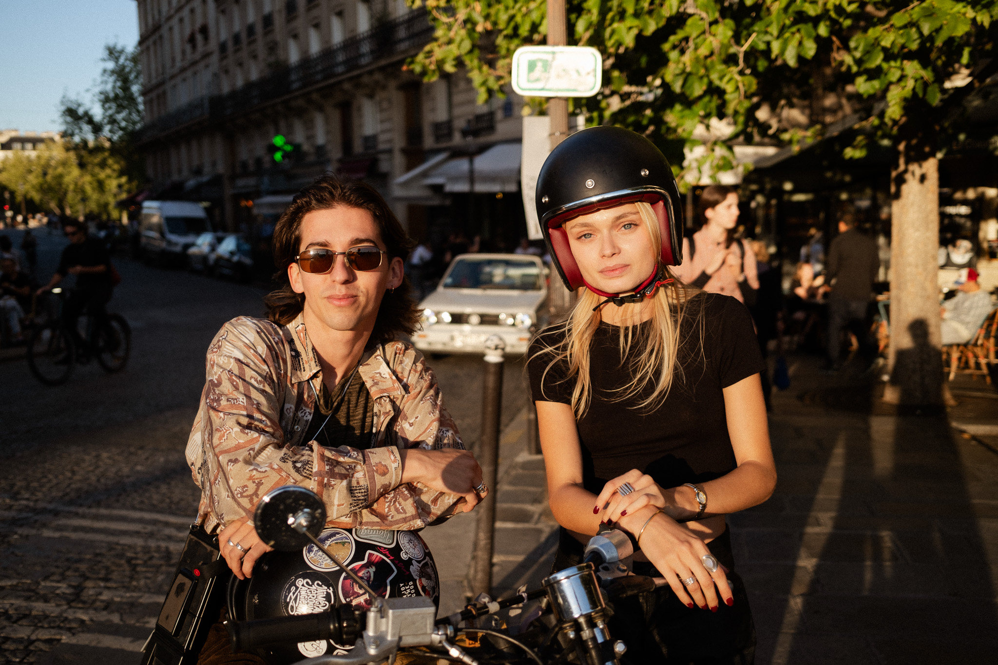 Couple leaning on a motorbike in low golden light, her helmet visor flipped up